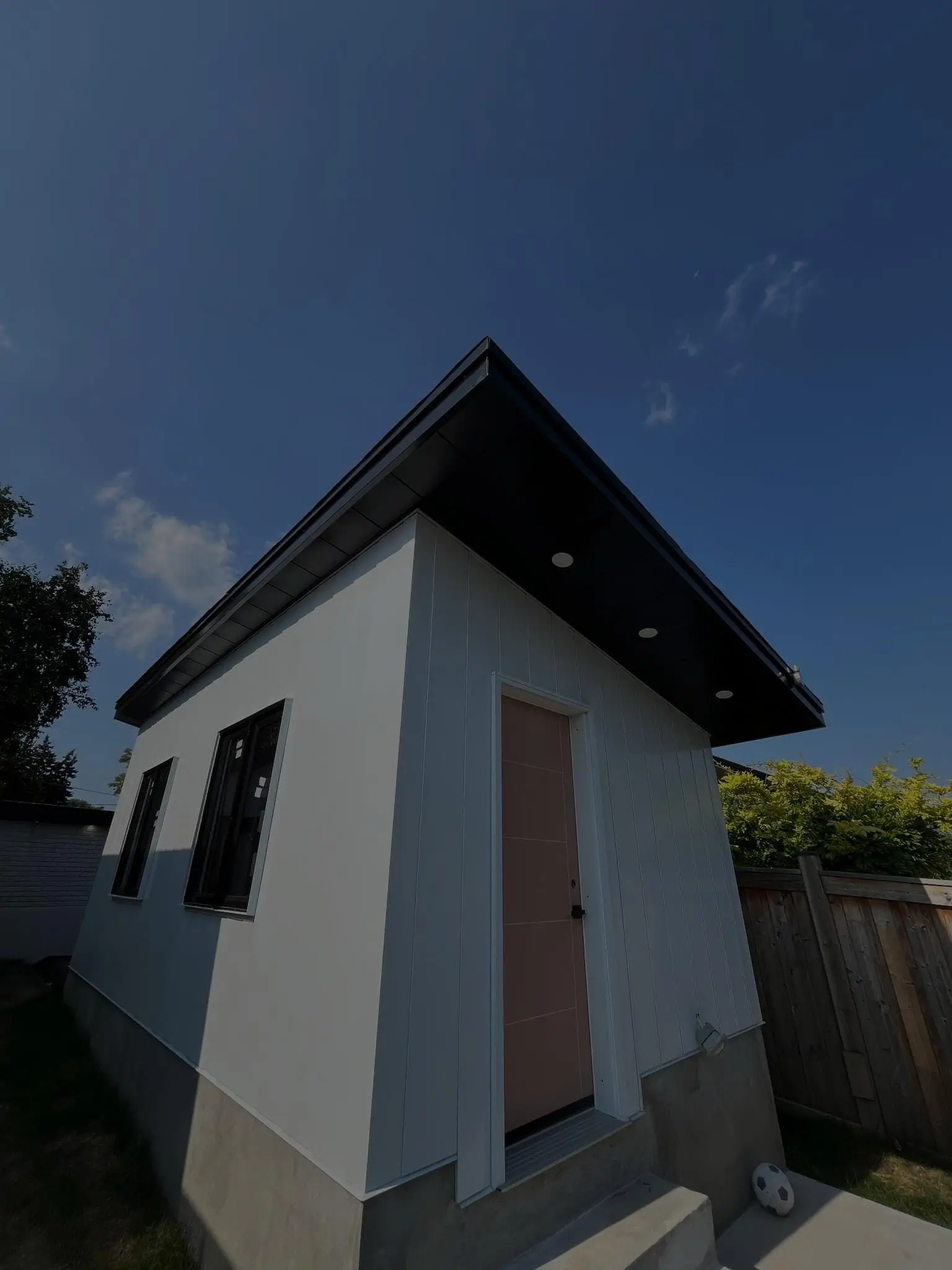 Backyard studio with white siding and a black metal roof edge