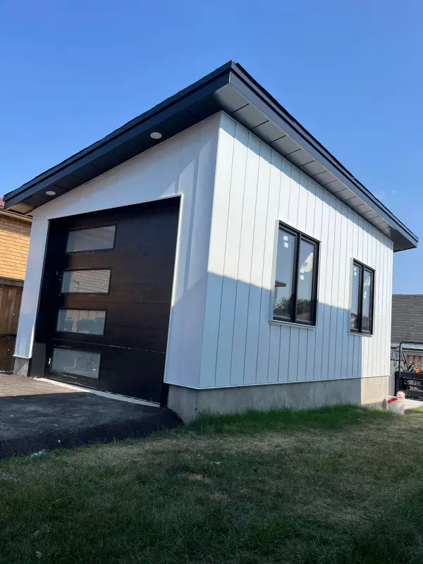 Accessory building with white vertical siding and a black flat roof edge