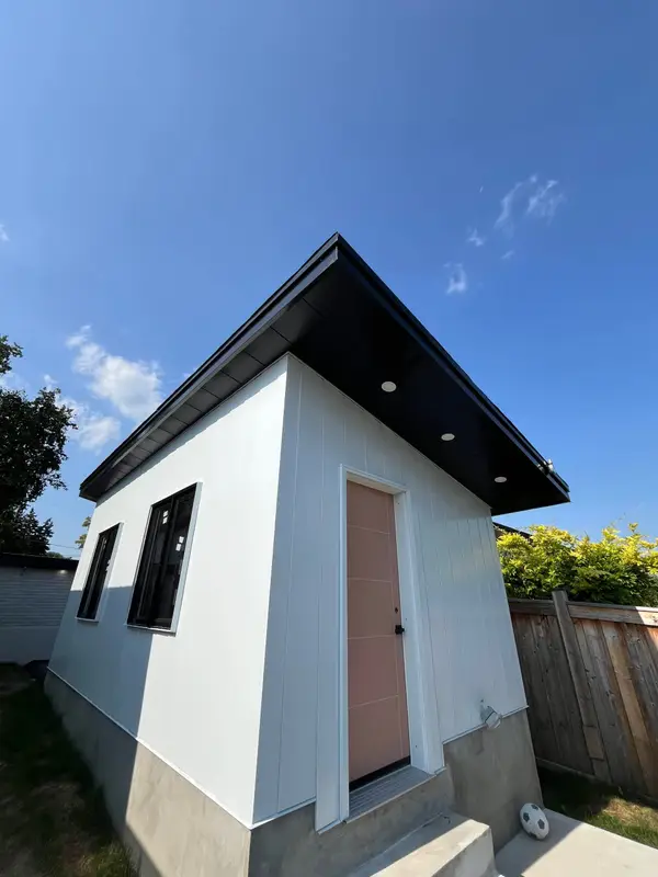 Small white backyard building with a black roof edge and soffit lights