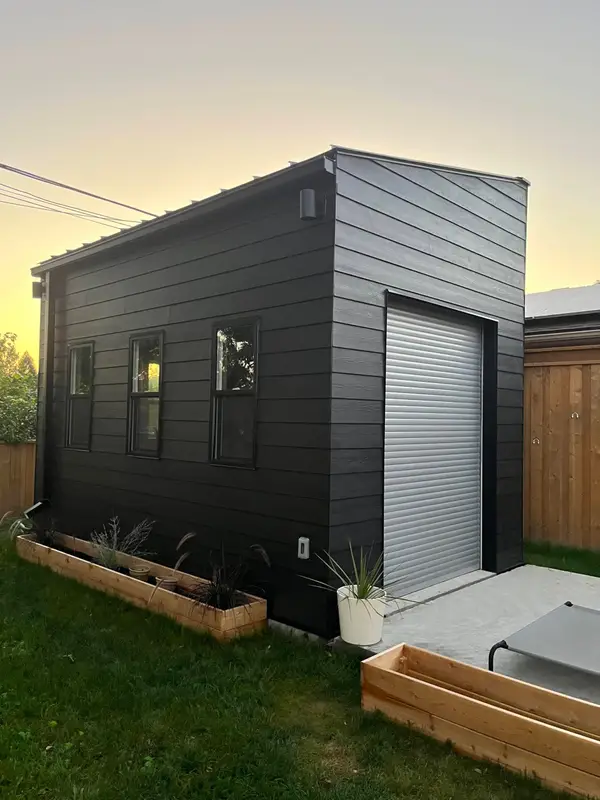 Black-sided backyard garage with a roll-up door at sunset