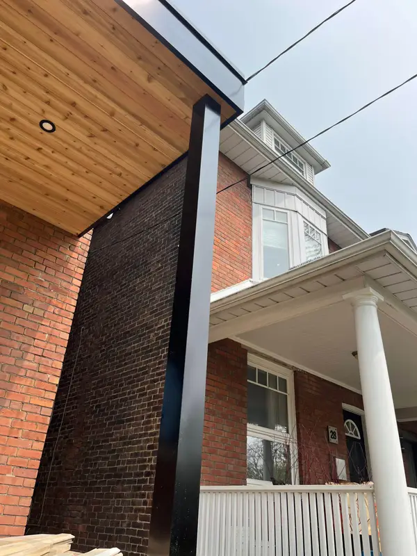 Black metal-wrapped post and wood soffit beside a brick porch