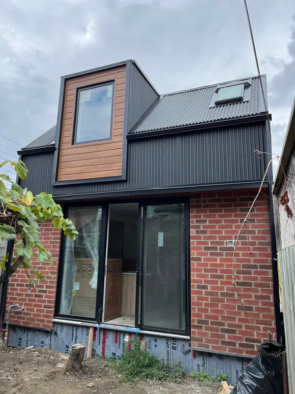 Brick addition with black metal siding and a wood-clad dormer