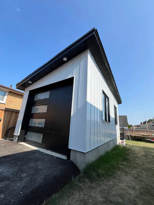 White-sided garage with a black roof edge and modern garage door