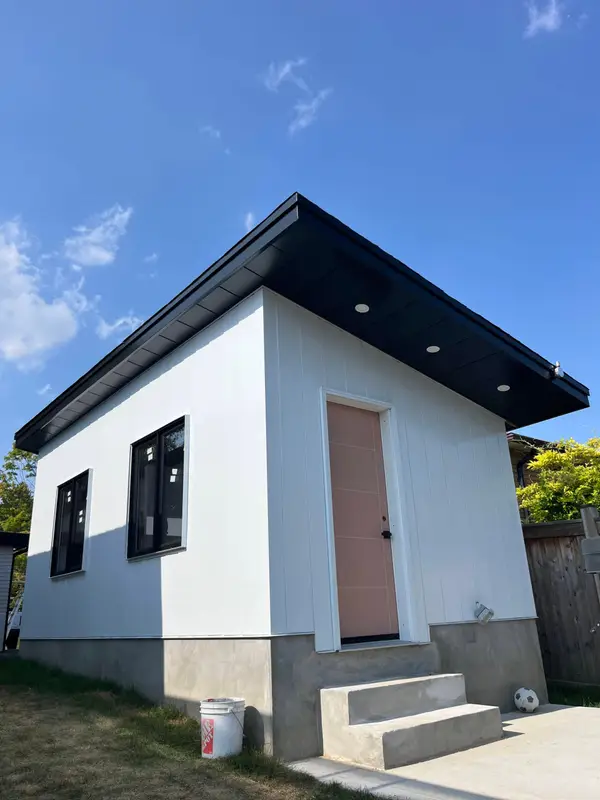 White backyard building with a black roof edge and pink door