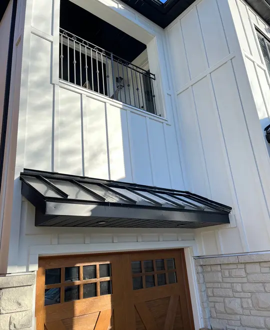 White board-and-batten home with a black standing-seam metal awning over wood garage doors
