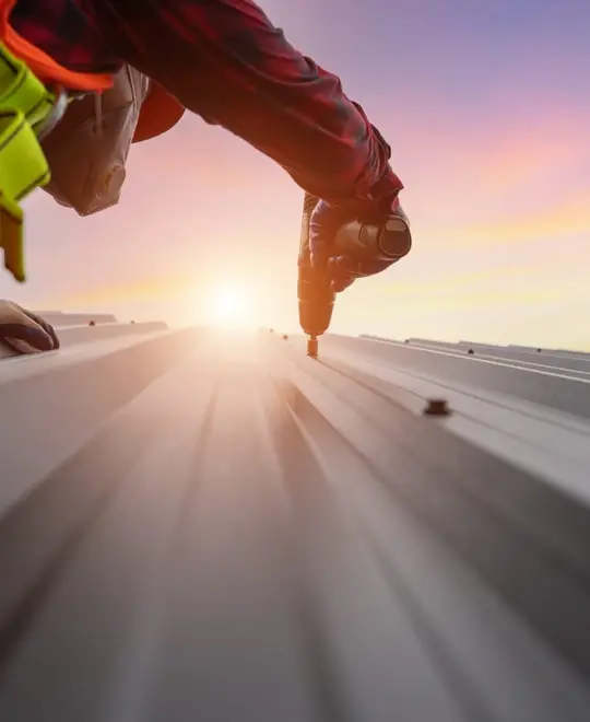 Roofer fastening metal roof panels at sunset